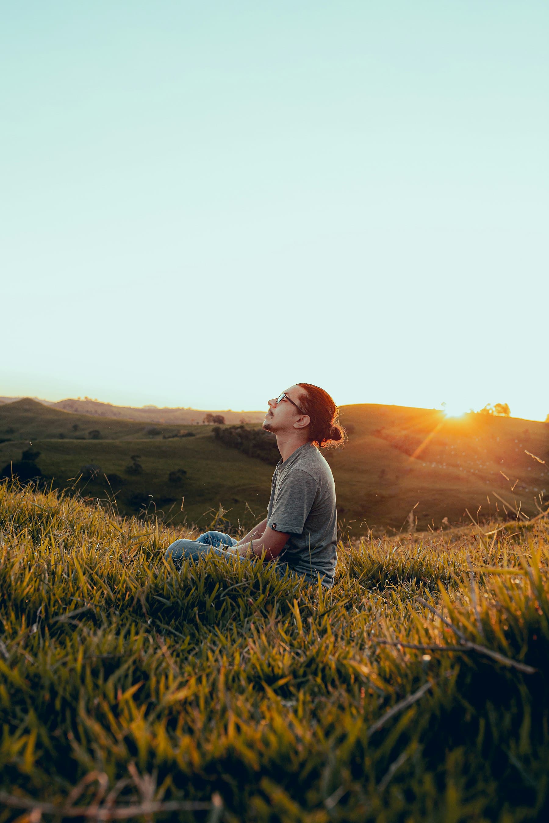 A man sitting in a meadow at sunrise, looking at the sky